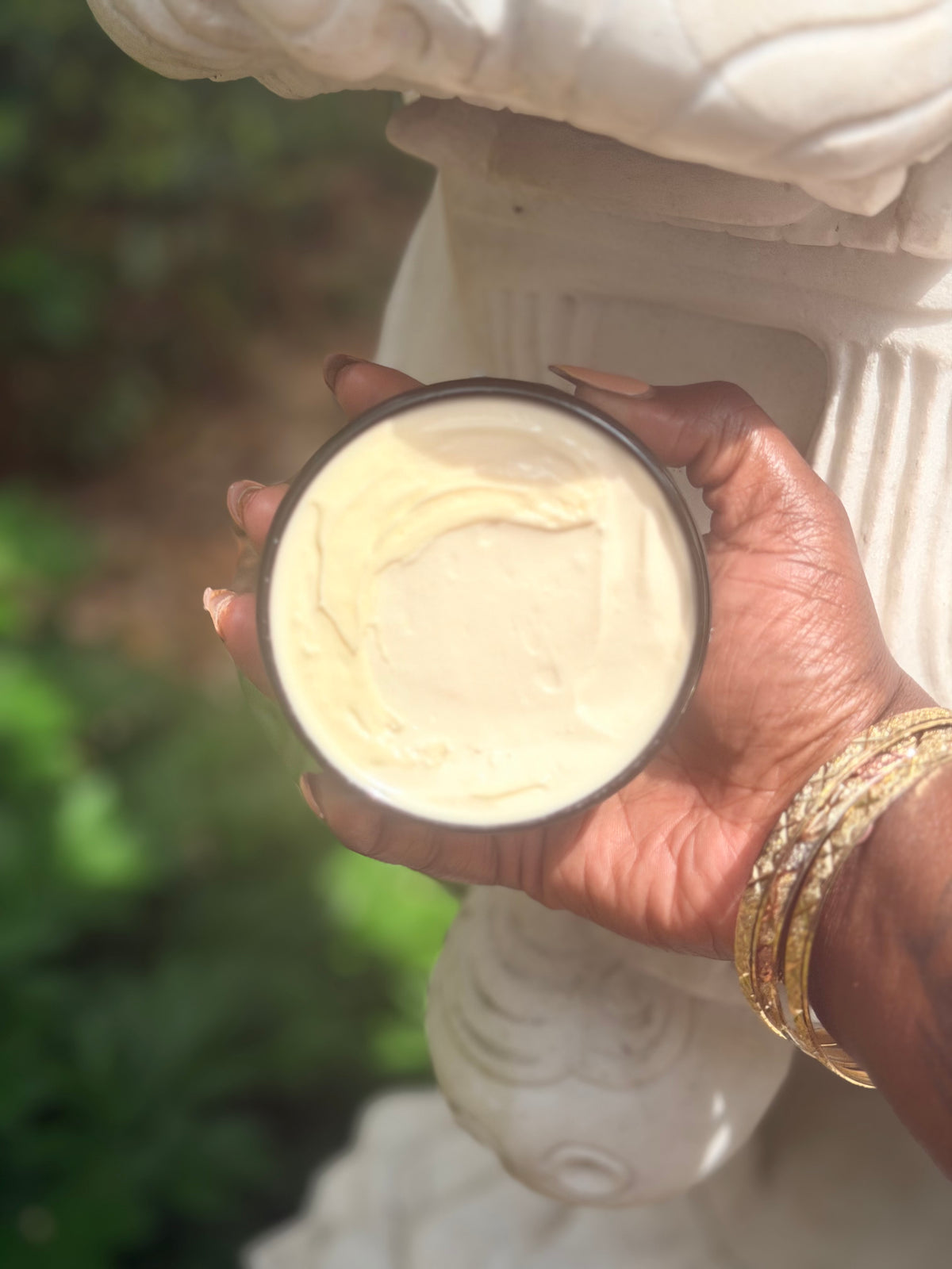 Hand holding a container of cream with a blurred natural background