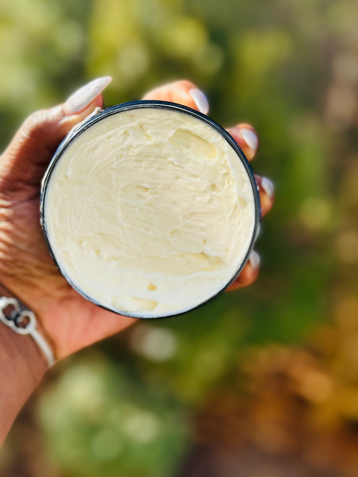 Hand holding a container of whipped creamy cream with a blurred natural background